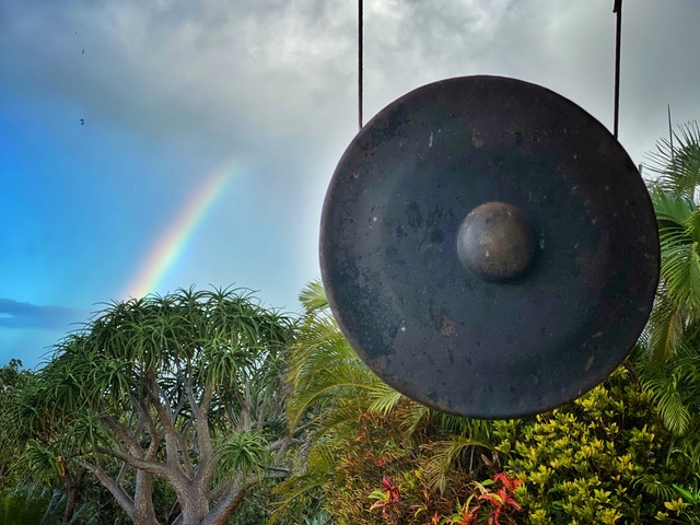 Rainbow in the sky over green trees and a gong